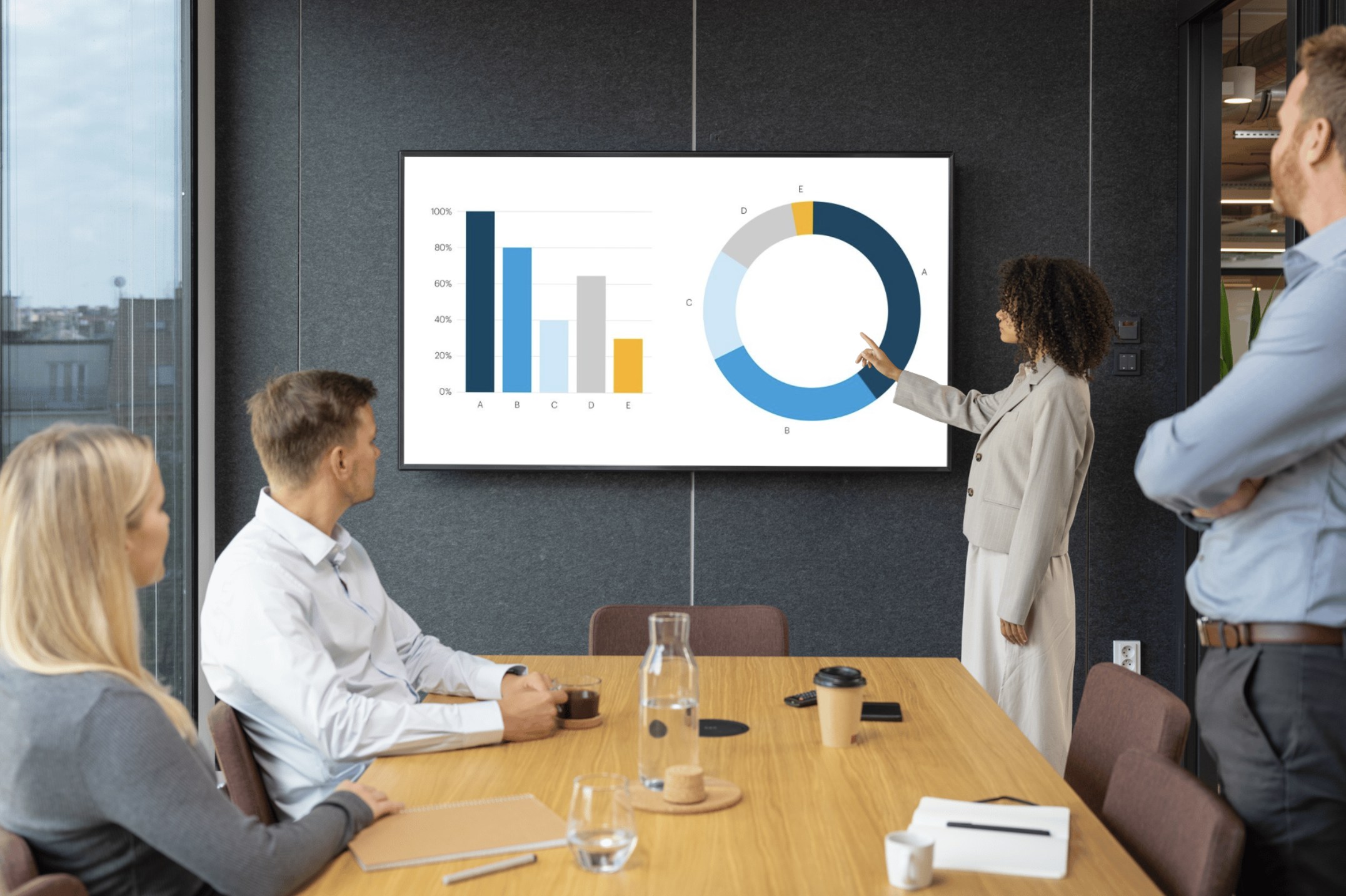 Businesswoman presenting bar and donut charts on a screen to colleagues during a meeting in a modern office.