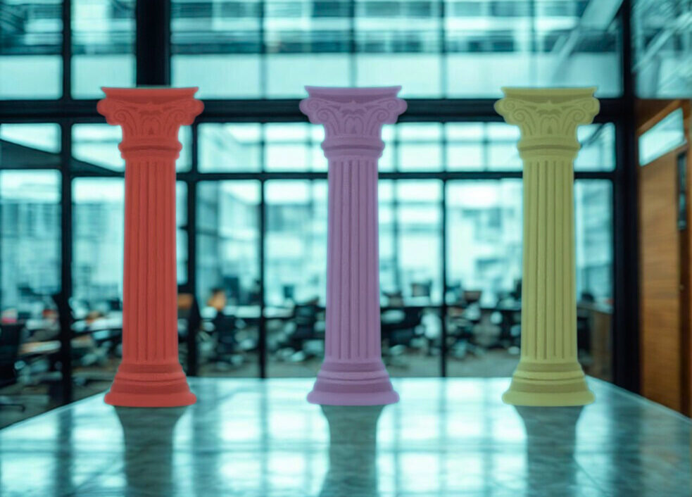 Three colorful columns, one red, one purple, and one yellow, standing on a reflective surface in a modern office space with large windows.